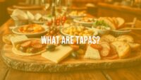 Assortment of Spanish tapas on a wooden table, vibrant colors, olives, cheese, chorizo, bread, cozy bar setting, social dining atmosphere, realistic.